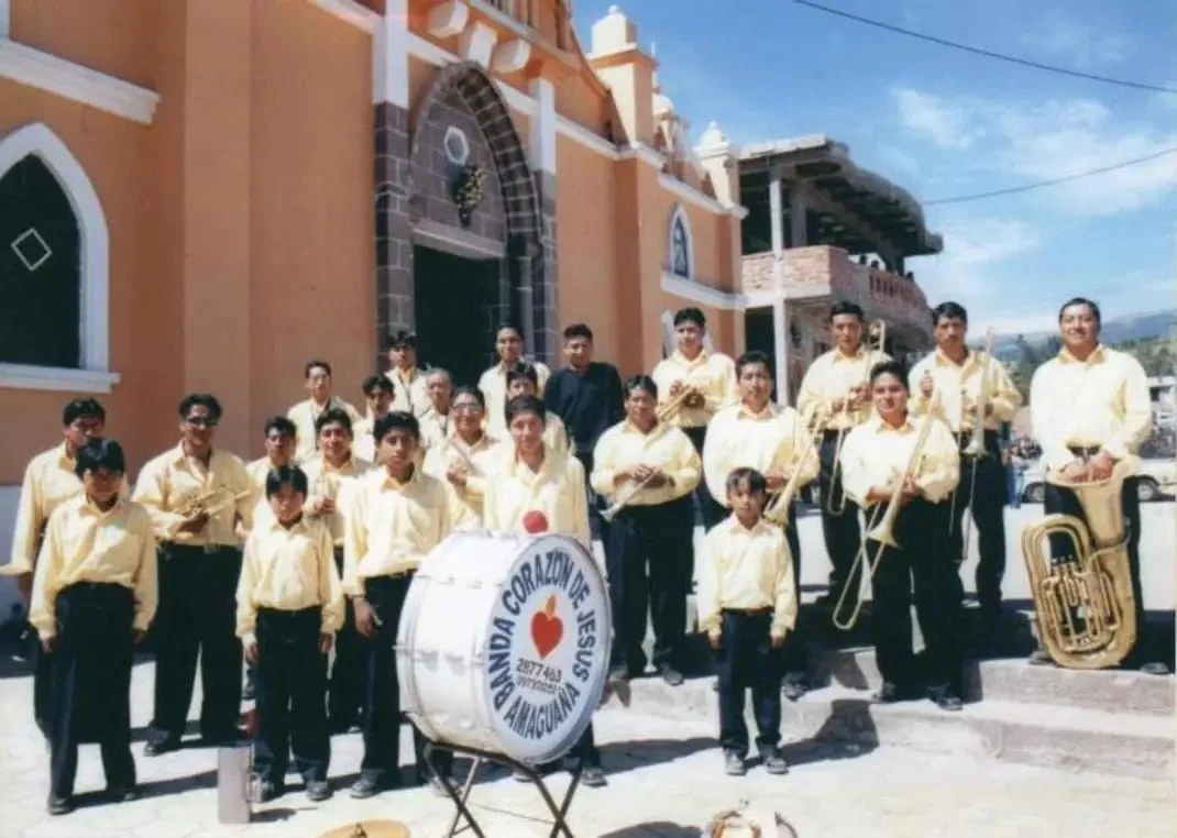 Banda Corazón de Jesús de Amaguaña con instrumentos frente a una iglesia.